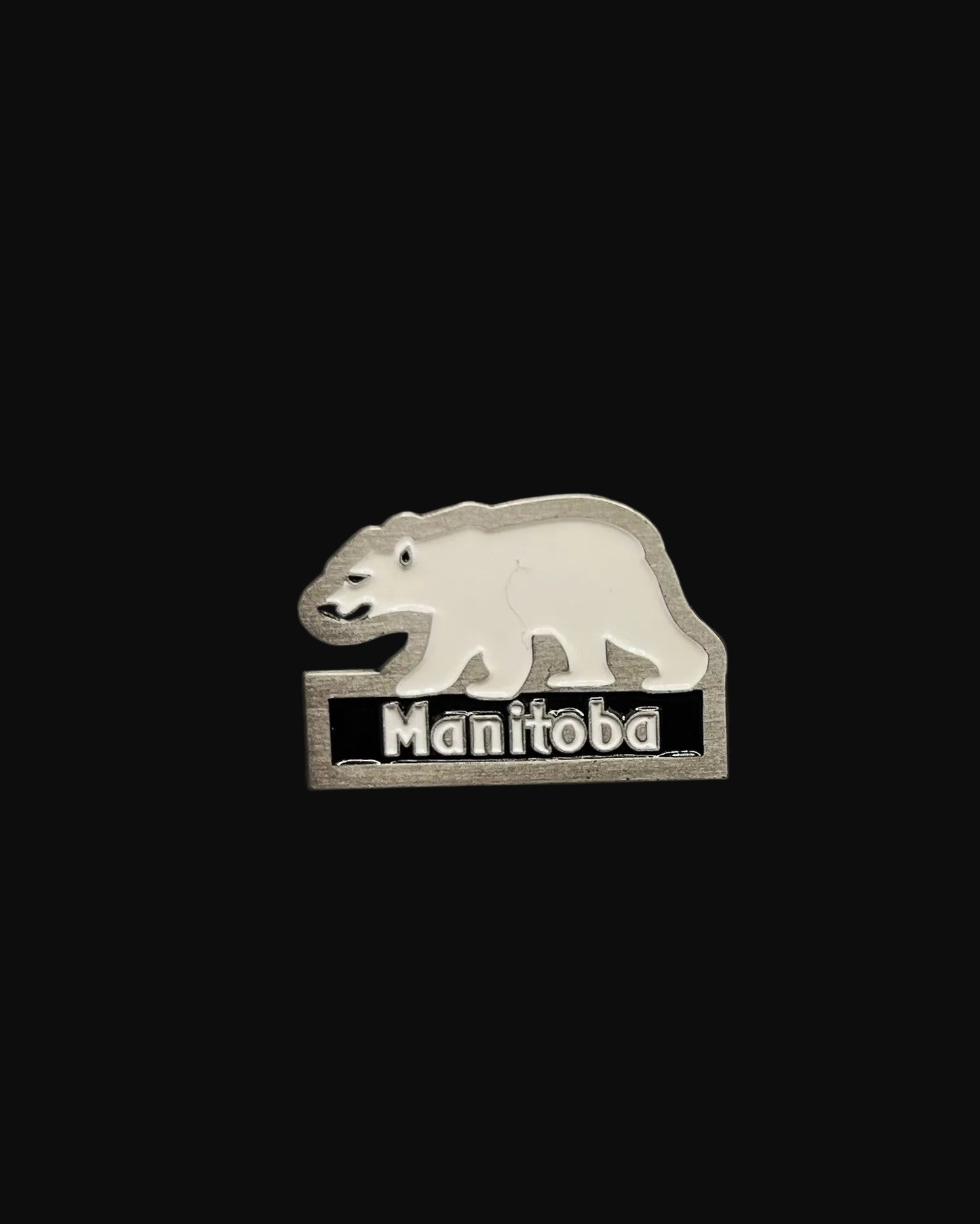A silver-colored lapel pin shaped like a polar bear with the word 'MANITOB' below it.